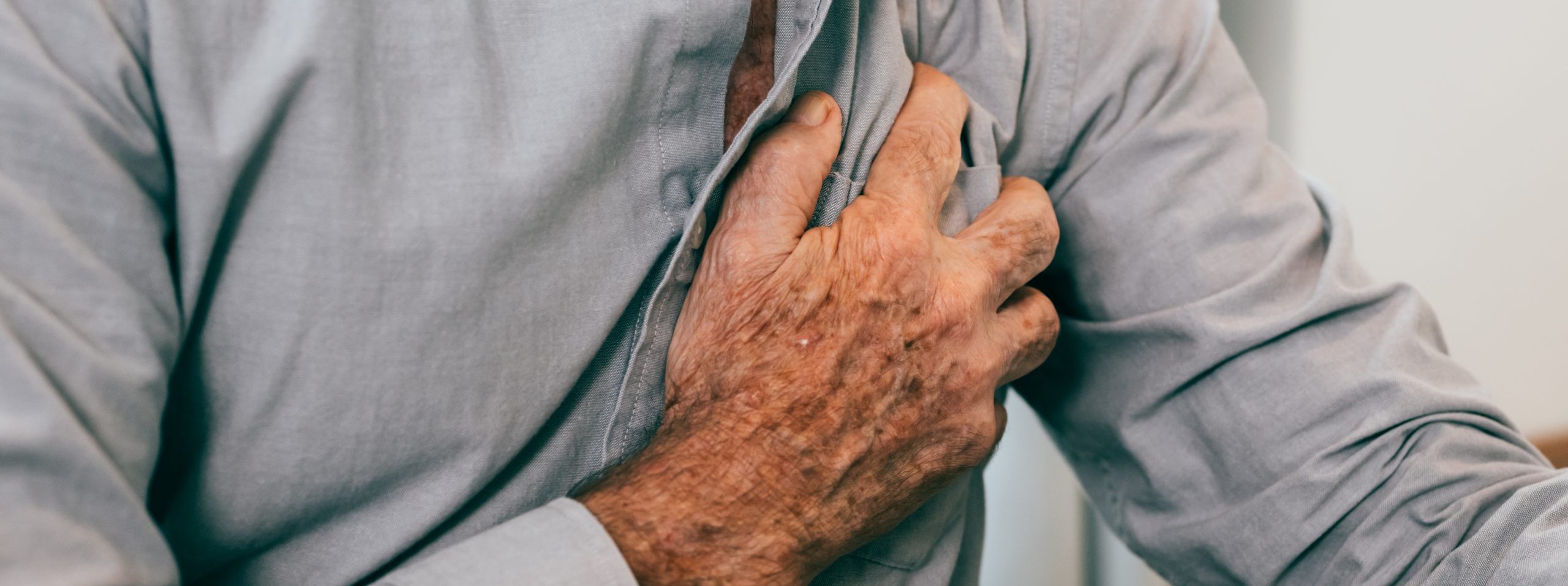 Senior man holding hand on chest and suffering from heart problem at home